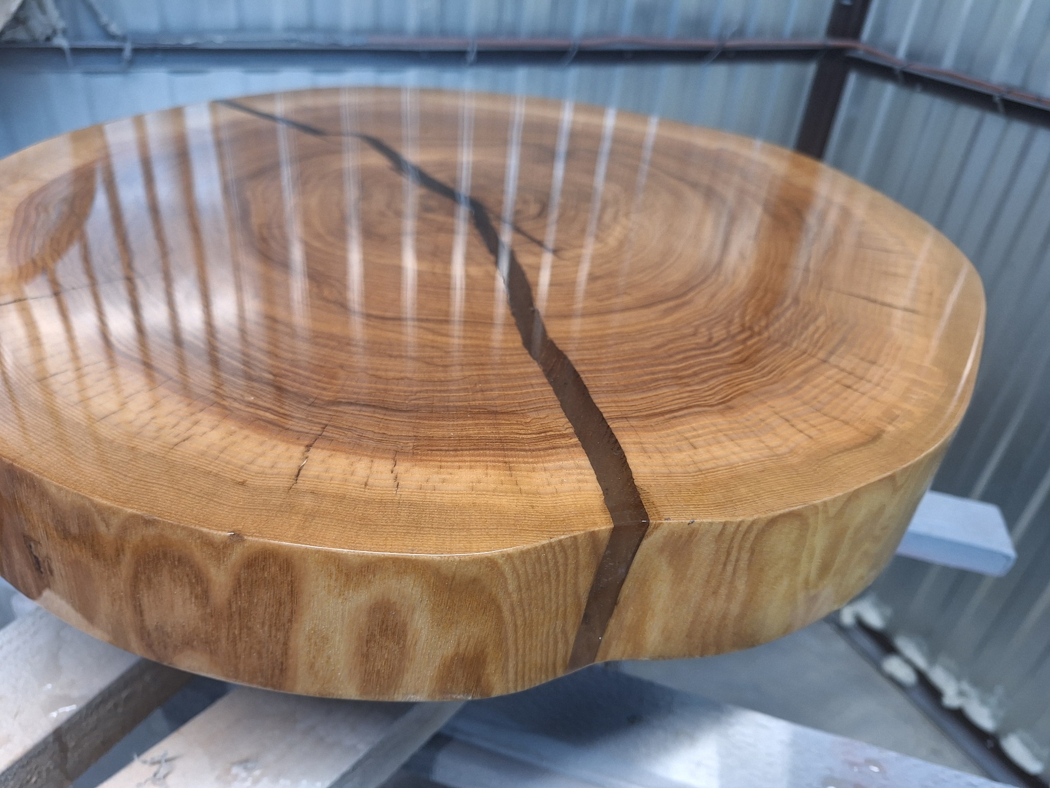 Okrągły blat stołu z drewna z żywicą epoksydową wypełniającą pęknięcie, ukazujący unikalne słoje i naturalny rysunek drewna. Blat jest polerowany i błyszczący.