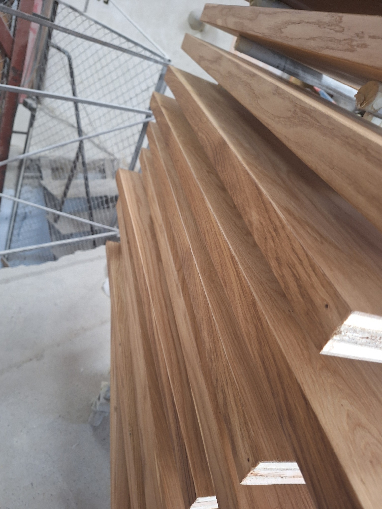 Drewniane stopnie schodów z widoczną strukturą drewna, ułożone spiralnie, z metalową barierką w tle. Ujęcie z góry, podkreślające detale wykończenia.