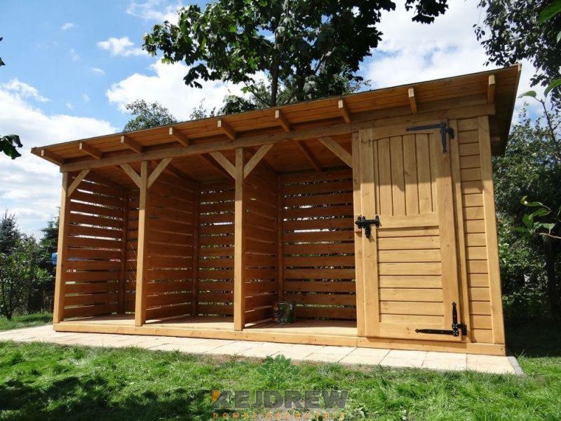 Drewniana wiata na drewno opałowe z trzema przegrodami, zamykana na czarne, metalowe okucia, umieszczona na betonowej płycie w ogrodzie.