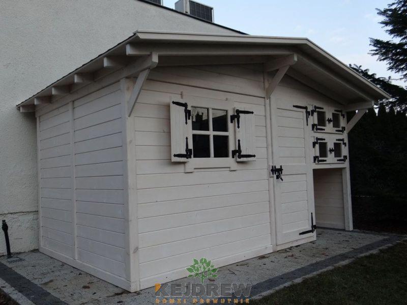 Biała, drewniana altana ogrodowa z oknem z okiennicami i dwuskrzydłowymi drzwiami, umieszczona na szarym brukowanym podłożu obok budynku mieszkalnego.