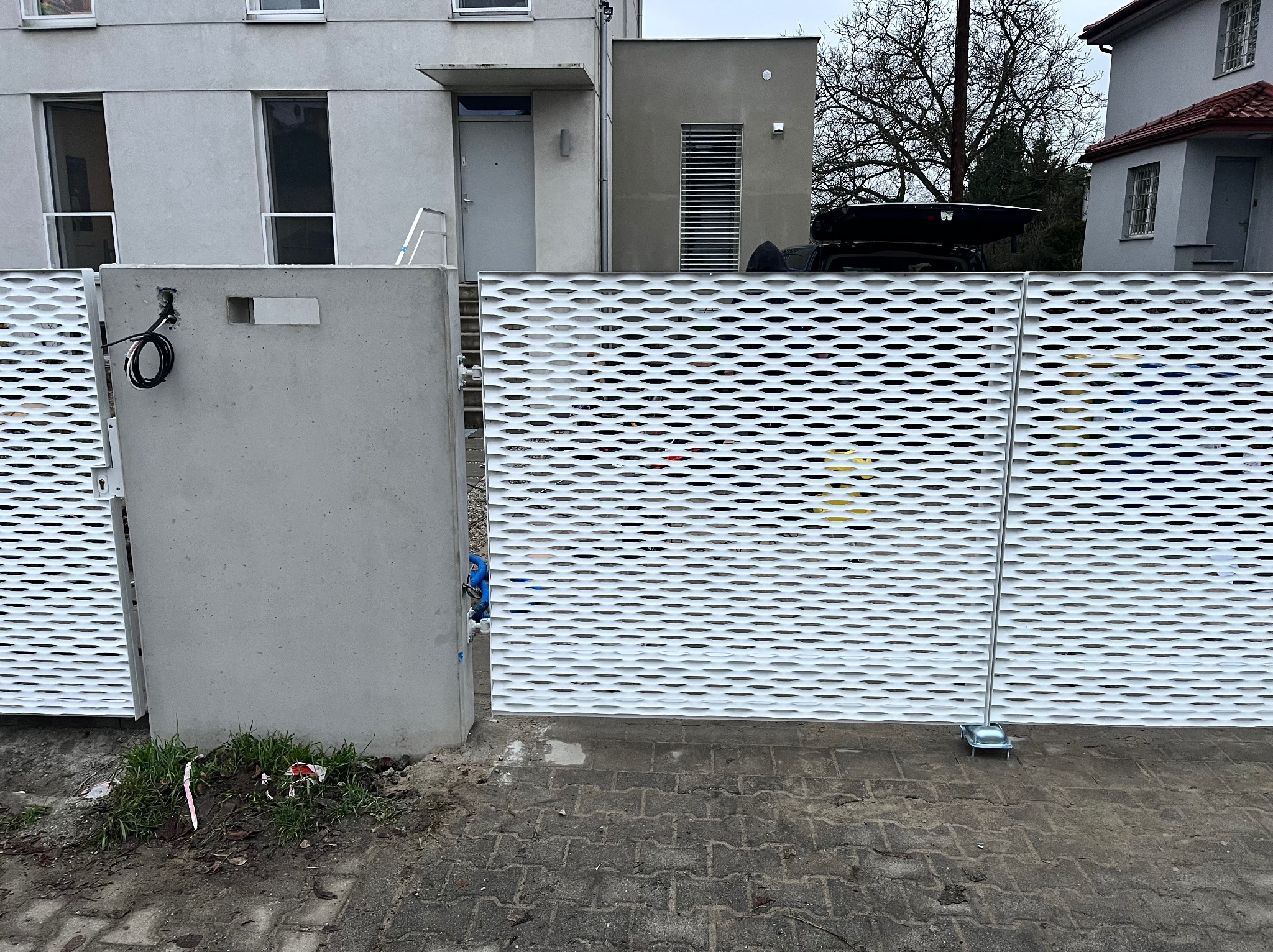 Nowoczesna brama wjazdowa z aluminiową siatką fasadową i stalową ramą, zabezpieczona cynkiem i lakierowana proszkowo, na tle budynku mieszkalnego.