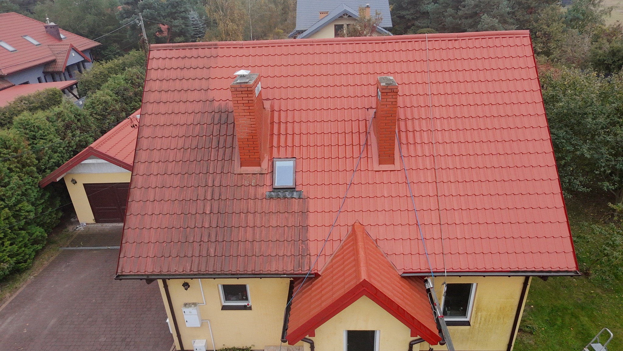 Częściowo umyty, czerwony dach z dachówki ceramicznej, widoczna różnica w czystości, dwa kominy z cegły, żółta elewacja domu, ujęcie z góry.