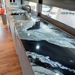 Bednarz & Stone Tomasz Bednarz - Czarno-biały blat kamienny z połyskiem, zamontowany w kuchni z oknem. Widoczny zlew i bateria. Blat o unikalnym wzorze przypominającym marmur.