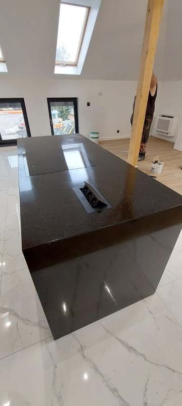 Ciemny blat kamienny z gniazdkami w wyspie kuchennej, widok z góry, w jasnym wnętrzu. Realizacja w Piławie Górnej.