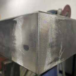 Usługi ślusarsko-spawalnicze Ciesiółka Jacek - Szlifowany, metalowy narożnik z widocznymi śladami obróbki i tęczowymi refleksami światła. W tle szlifierka kątowa.