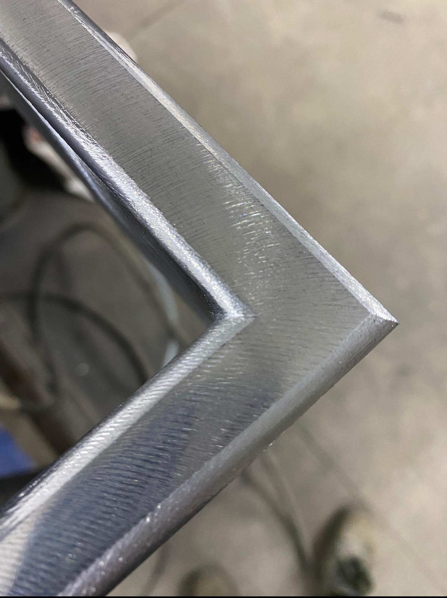 Szczegółowe ujęcie kąta spawanej ramy z metalu o srebrzystym odcieniu, ukazujące precyzję wykonania i gładką powierzchnię spoiny.