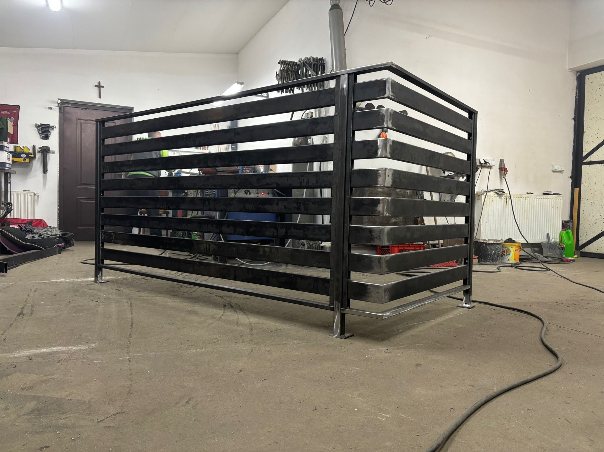 Surowa, metalowa konstrukcja z poziomych profili w warsztacie. Widoczne ślady obróbki, spawania. W tle narzędzia i wyposażenie warsztatowe.