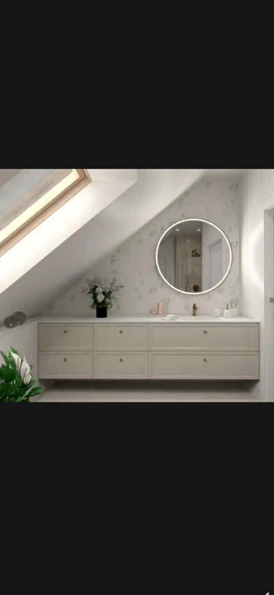 Jasna łazienka na poddaszu ze skośnym oknem dachowym. Umywalka z szafkami, okrągłe lustro z podświetleniem LED i delikatny wzór na ścianie.