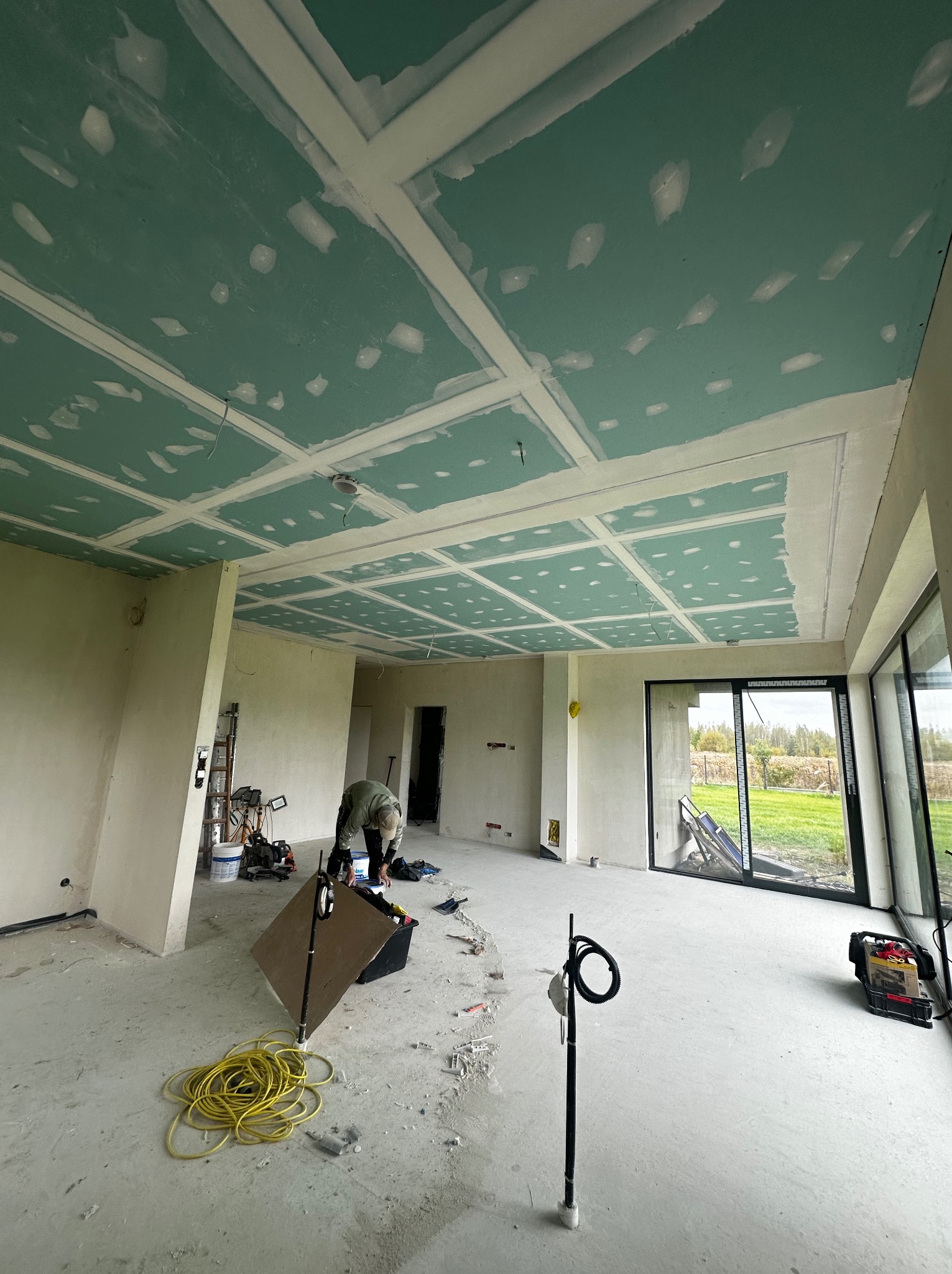 Montaż sufitu podwieszanego z płyt w nowym domu. Widoczne narzędzia i instalacje. Sufit w trakcie szpachlowania, z widoczną siatką wzmacniającą na łączeniach.