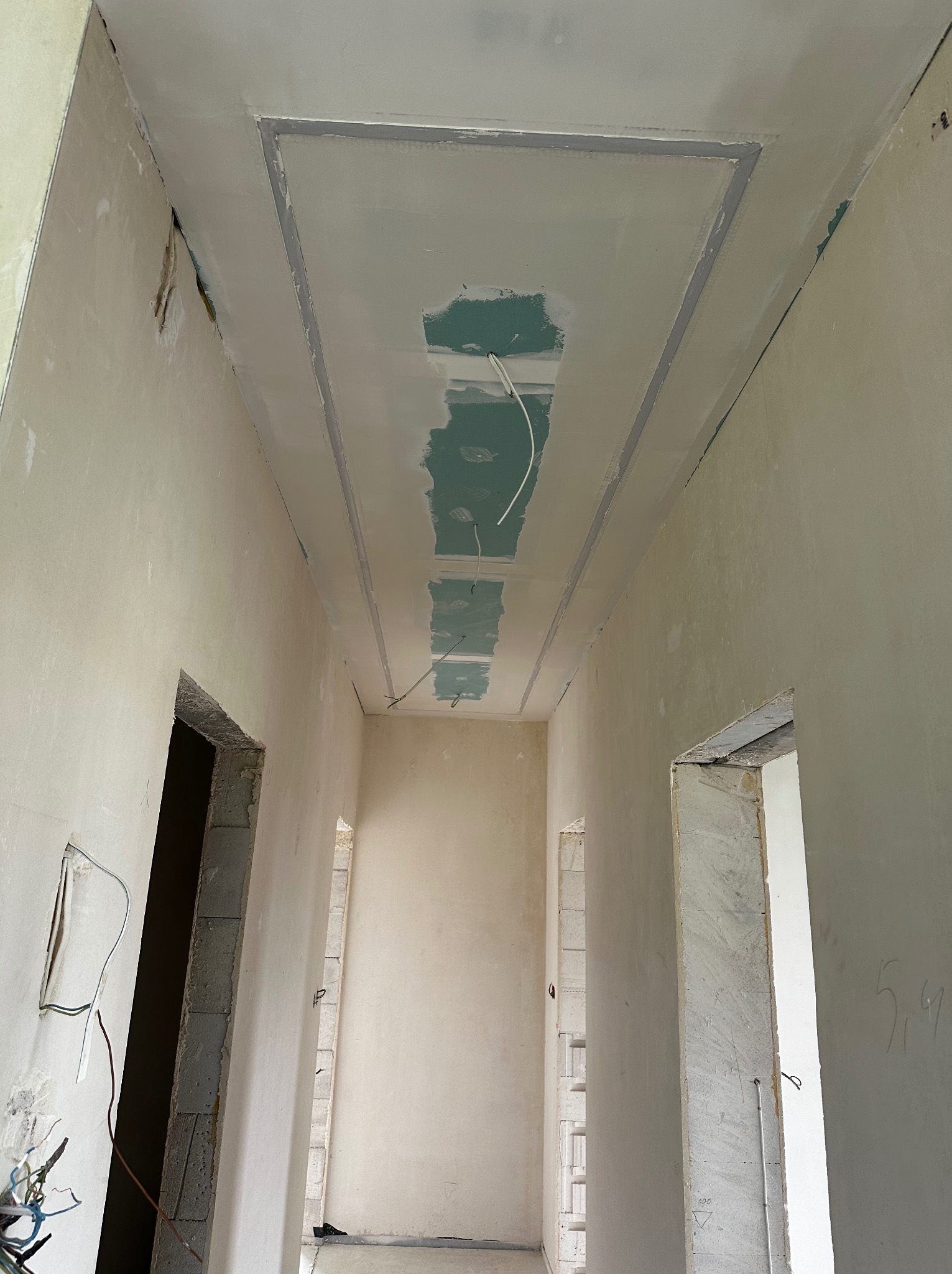 Sufit z obniżeniem i szpachlowaniem w korytarzu, widoczne kable i niedokończone ściany. Ujęcie z dołu, perspektywa wnętrza w trakcie prac.