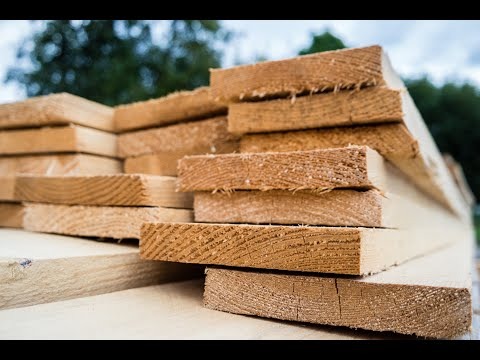 Stos tarcicy budowlanej z widocznym rysunkiem słojów drewna, ułożony na jasnej powierzchni. Świeżo przetarte deski z delikatnymi zadziorami. Tło rozmyte, zielone.