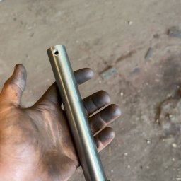 Wiktor Gronowski Usługi Ślusarskie - Polerowany, metalowy trzpień z otworem w dłoni ślusarza, widoczne ślady pracy. Tło warsztatowe z elementami metalowymi.