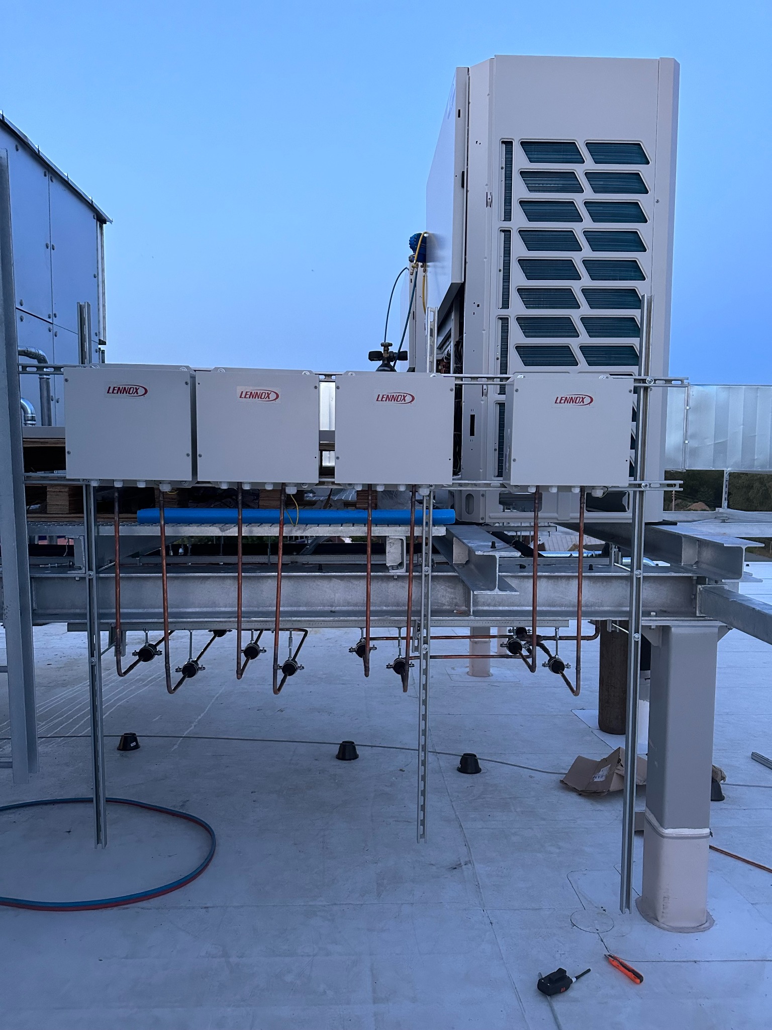 Instalacja klimatyzacji Lennox na dachu budynku, widoczne cztery skrzynki sterownicze i jednostka zewnętrzna. Miedziane rury i metalowa konstrukcja wsporcza.