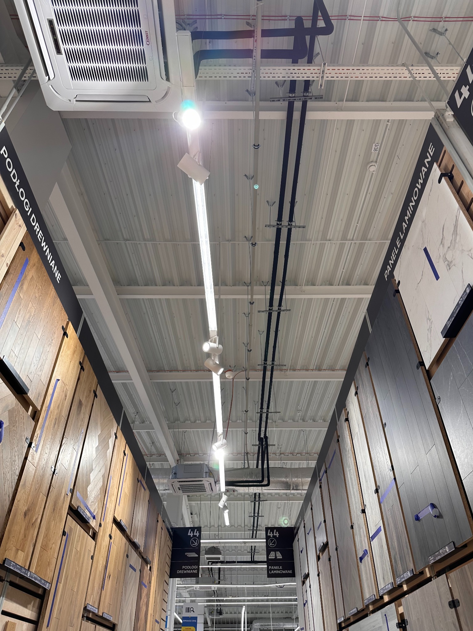 Kasetonowa klimatyzacja sufitowa Lennox w markecie budowlanym, widok z dołu na instalacje i oświetlenie, panele podłogowe po bokach.