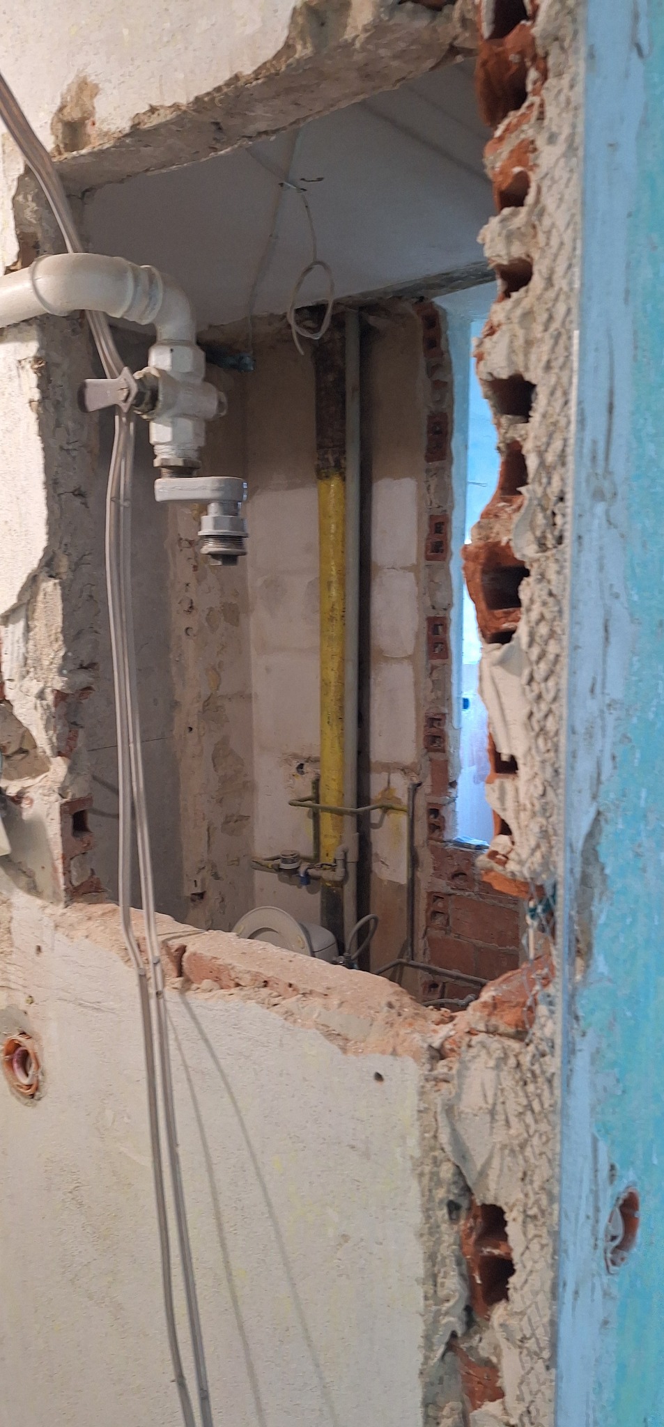 Fragment ściany z instalacją hydrauliczną i elektryczną w trakcie remontu. Widoczne odsłonięte cegły i przewody. Prace przygotowawcze do wykończenia wnętrza.