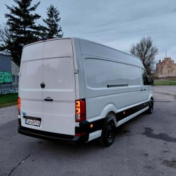 Michał Wojdas Usługi Transportowo - Kurierskie - Biały furgon Volkswagen Crafter z czarnymi felgami, zaparkowany na tle zamku i drzew. Widok z tyłu, tablica rejestracyjna SW 68954.