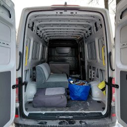 Michał Wojdas Usługi Transportowo - Kurierskie - Wnętrze białego busa z otwartymi drzwiami, częściowo załadowane meblami, torbami i kartonami. Widoczny śnieg na zewnątrz pojazdu.
