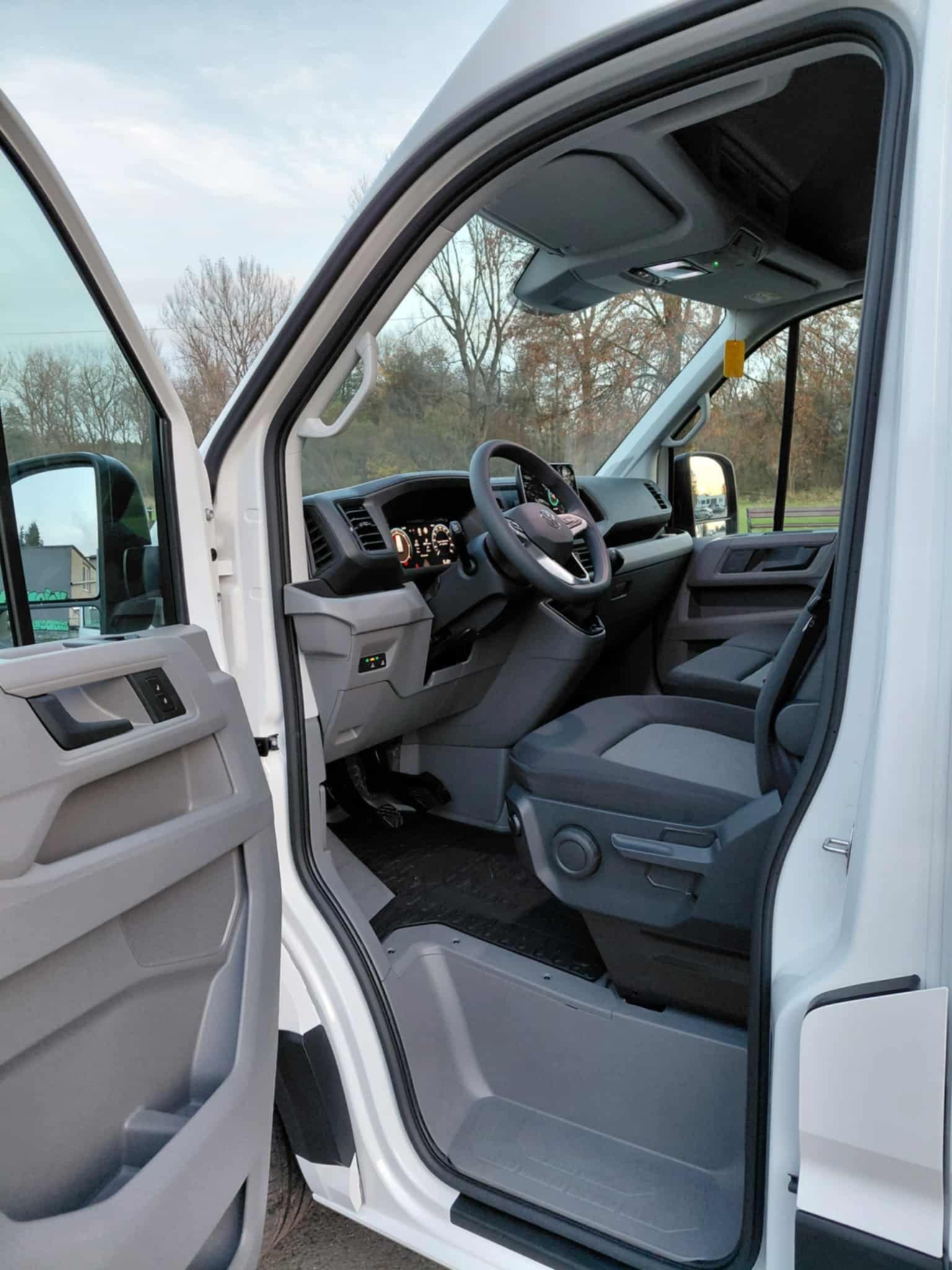 Wnętrze białego busa z otwartymi drzwiami w Siewierzu. Widoczna deska rozdzielcza, kierownica i fotele. Idealny do transportu osób lub przeprowadzek.