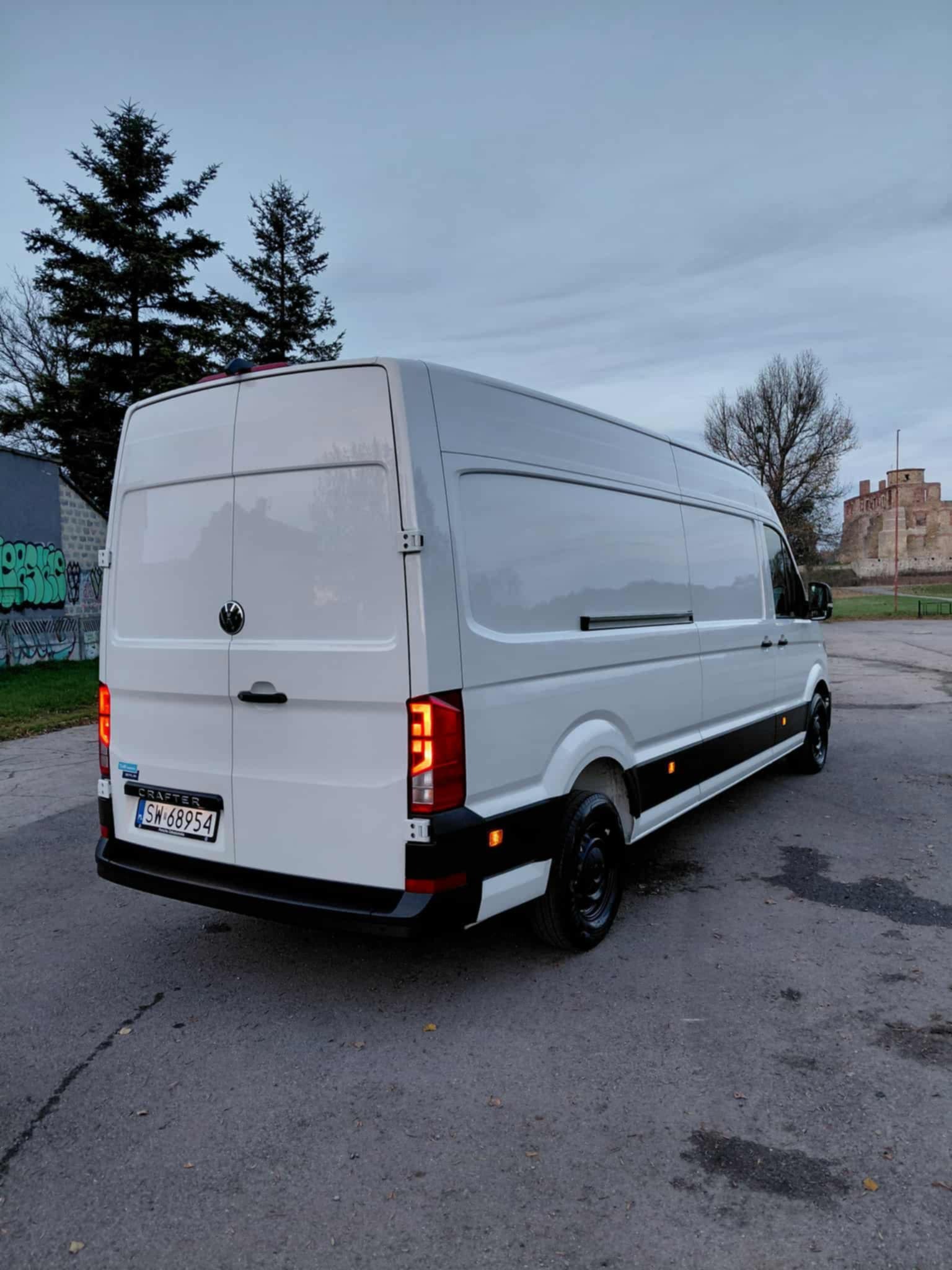 Biały bus Volkswagen Crafter z czarnymi felgami na tle zamku i drzew, widok z tyłu. Tablica rejestracyjna SW 68954.