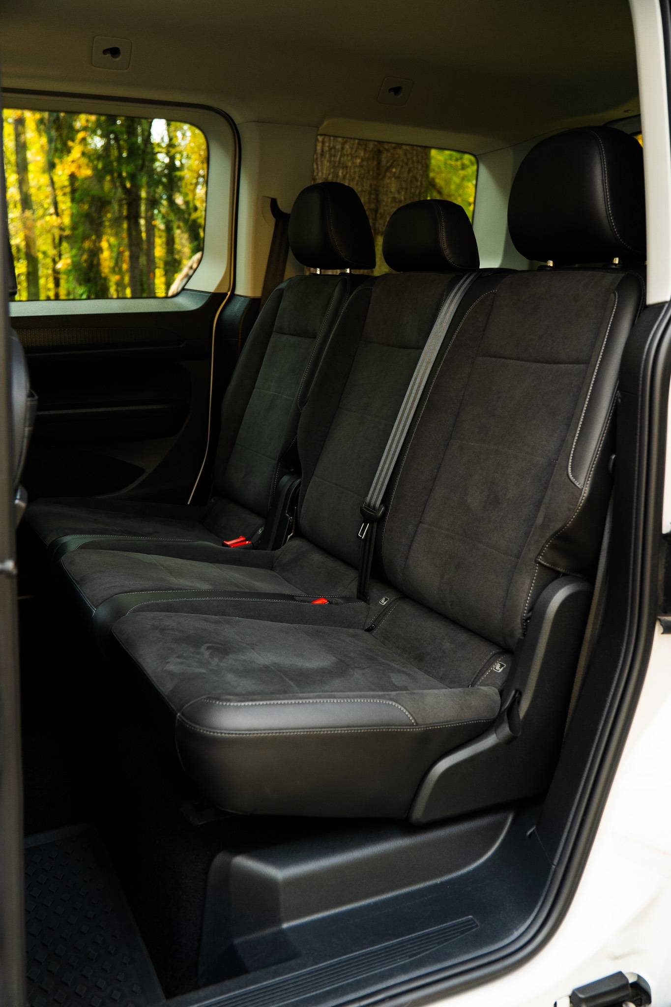Wnętrze busa z trzema rzędami czarnych, welurowych siedzeń, widok z otwartych drzwi na zieleń drzew za oknem. Czyste i zadbane wnętrze pojazdu.