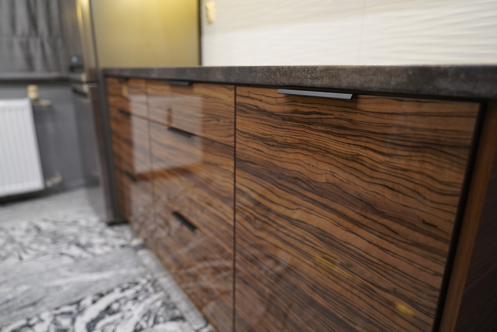 Fronty szafek kuchennych z egzotycznego drewna zebrano i blatem z ciemnego kamienia we Wrocławiu. Minimalistyczne uchwyty podkreślają nowoczesny design.