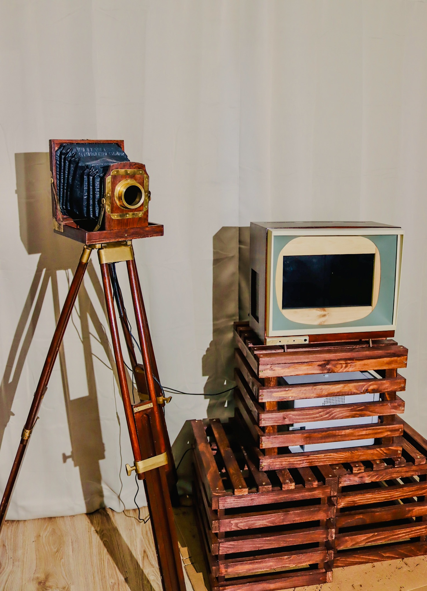 Stylizowana fotobudka z retro aparatem na drewnianym statywie i ekranem na skrzynkach, na tle kremowej tkaniny. Unikalny design i oświetlenie tworzą klimat vintage.