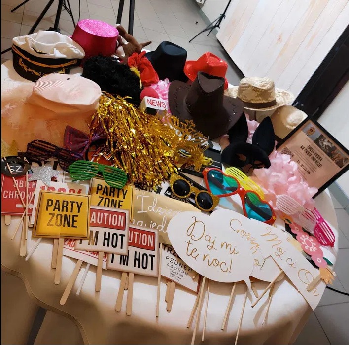 Różnorodne rekwizyty na stole: kapelusze, okulary, maski i tabliczki z napisami, gotowe do użycia podczas imprezy z fotobudką. Zestaw akcesoriów na wesołe zdjęcia.