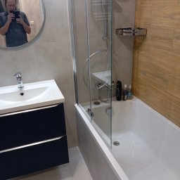 Ivan Vasyltsiv Vanbud - Nowoczesna łazienka z kabiną prysznicową, umywalką z szafką w kolorze granatowym i drewnopodobnymi płytkami na ścianie. W lustrze odbija się osoba robiąca zdjęcie.