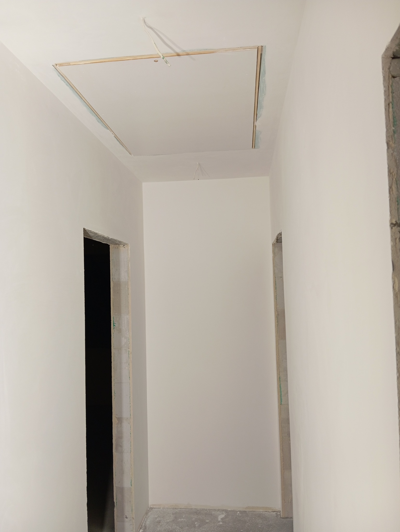 Białe ściany korytarza po szpachlowaniu i malowaniu, widoczne otwory drzwiowe bez ościeżnic i sufit z zamontowaną płytą karton-gips z otworem rewizyjnym.