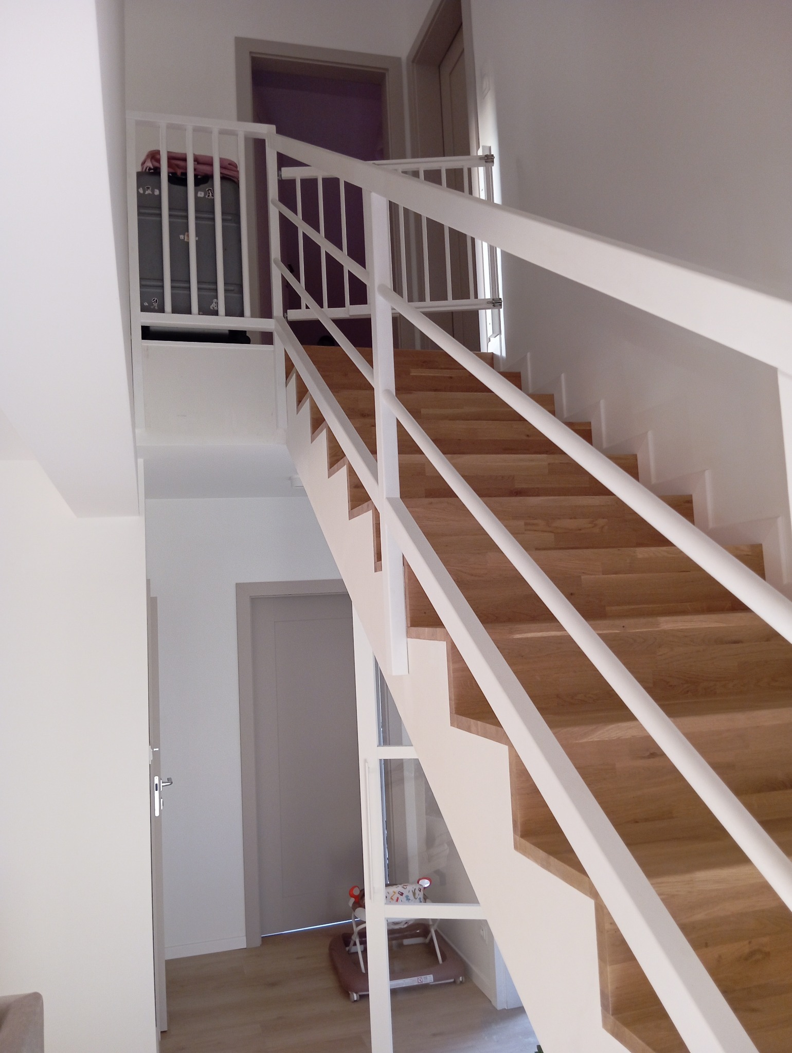 Nowoczesne schody drewniane z białymi balustradami w jasnym wnętrzu. Widoczny fragment pokoju dziecięcego z zabawkami. Minimalistyczny design.