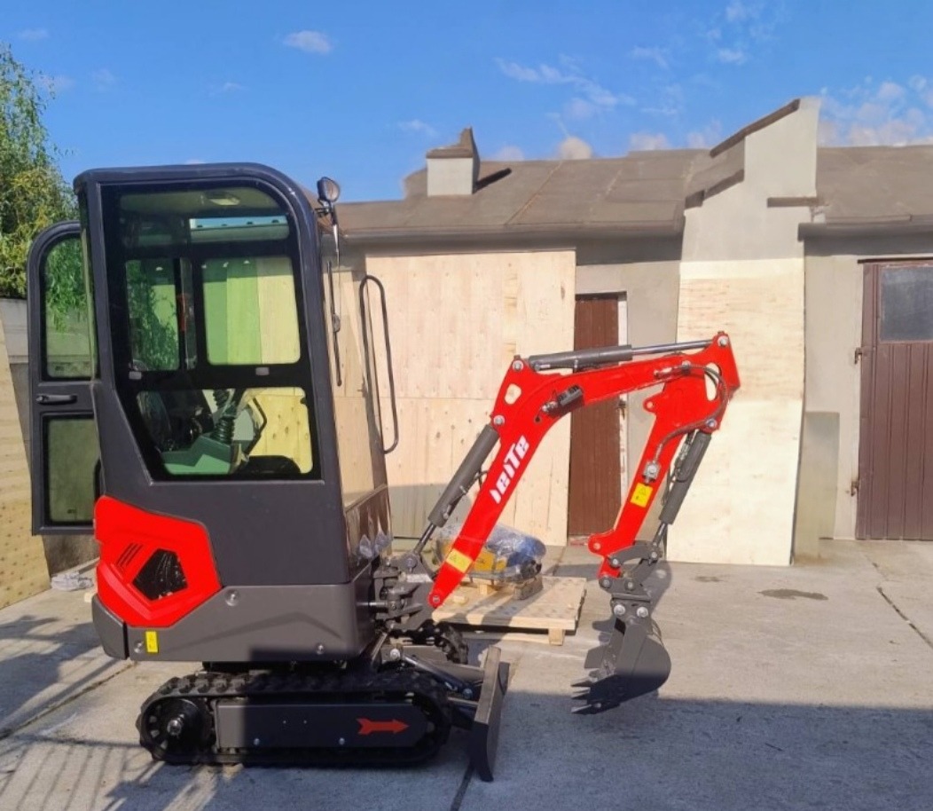 Czerwono-czarna mini koparka gąsienicowa IHIte na betonowym podłożu, z otwartą kabiną i widocznym ramieniem kopiącym, na tle budynku z drewnianą elewacją.