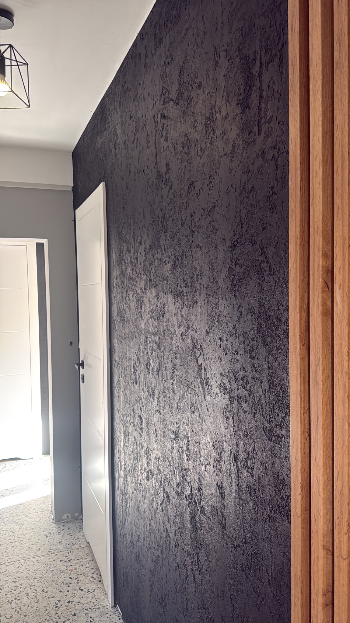 Ciemna ściana z efektem dekoracyjnym, pionowe drewniane panele, białe drzwi w tle. Nowoczesne wykończenie wnętrza z bliska.