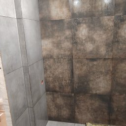 Dominik - Wykończona łazienka z szarymi i brązowymi płytkami na ścianach i podłodze. Widoczny fragment kuwety z narzędziami. Górne oświetlenie.