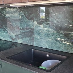 Dominik - Kuchnia z zielonym marmurem na ścianie, czarnym zlewem i płytą. Widoczne gniazdka elektryczne. Ujęcie z bliska, prezentujące detale wykończenia.