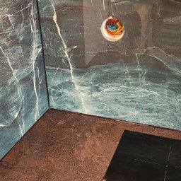 Dominik - Wykończona ściana i blat kuchenny z zielonego marmuru z widocznym gniazdkiem elektrycznym. Nowoczesny design, eleganckie wykończenie.