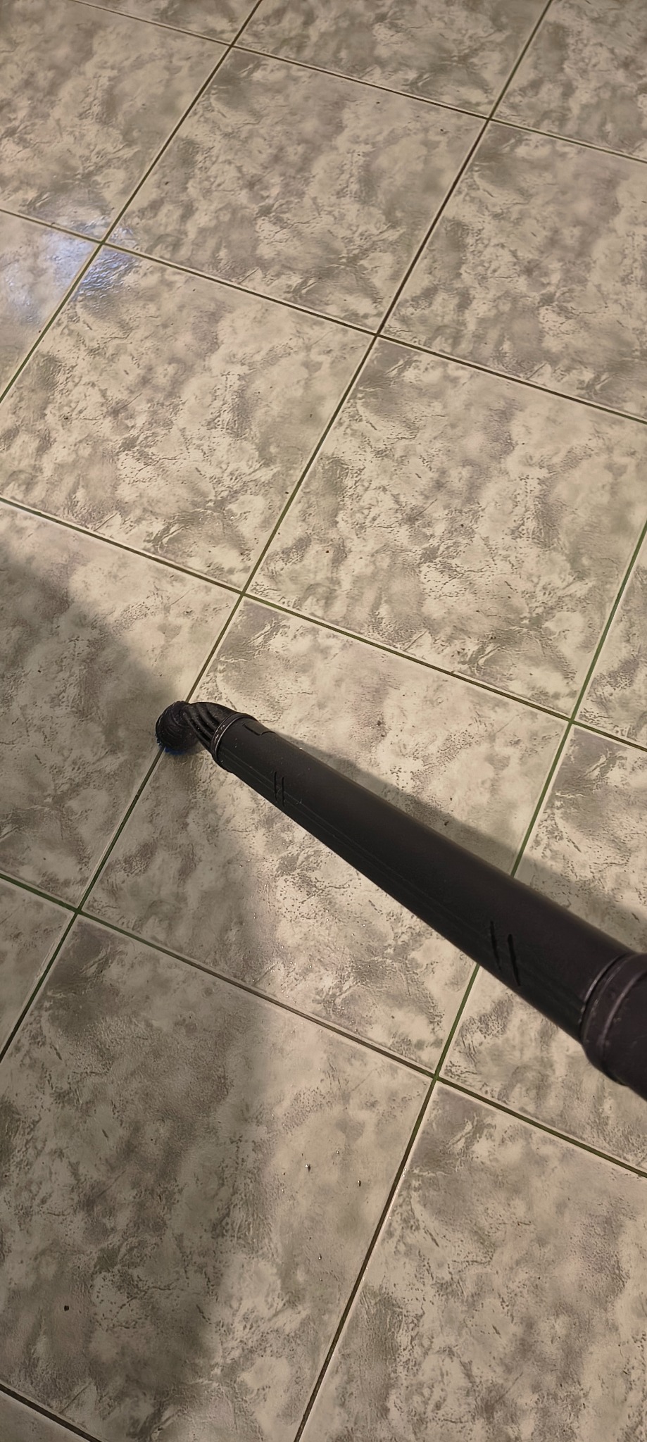 Dysza odkurzacza parowego na jasnych, kwadratowych płytkach podłogowych z delikatnym wzorem. Widok z góry, lekki cień.