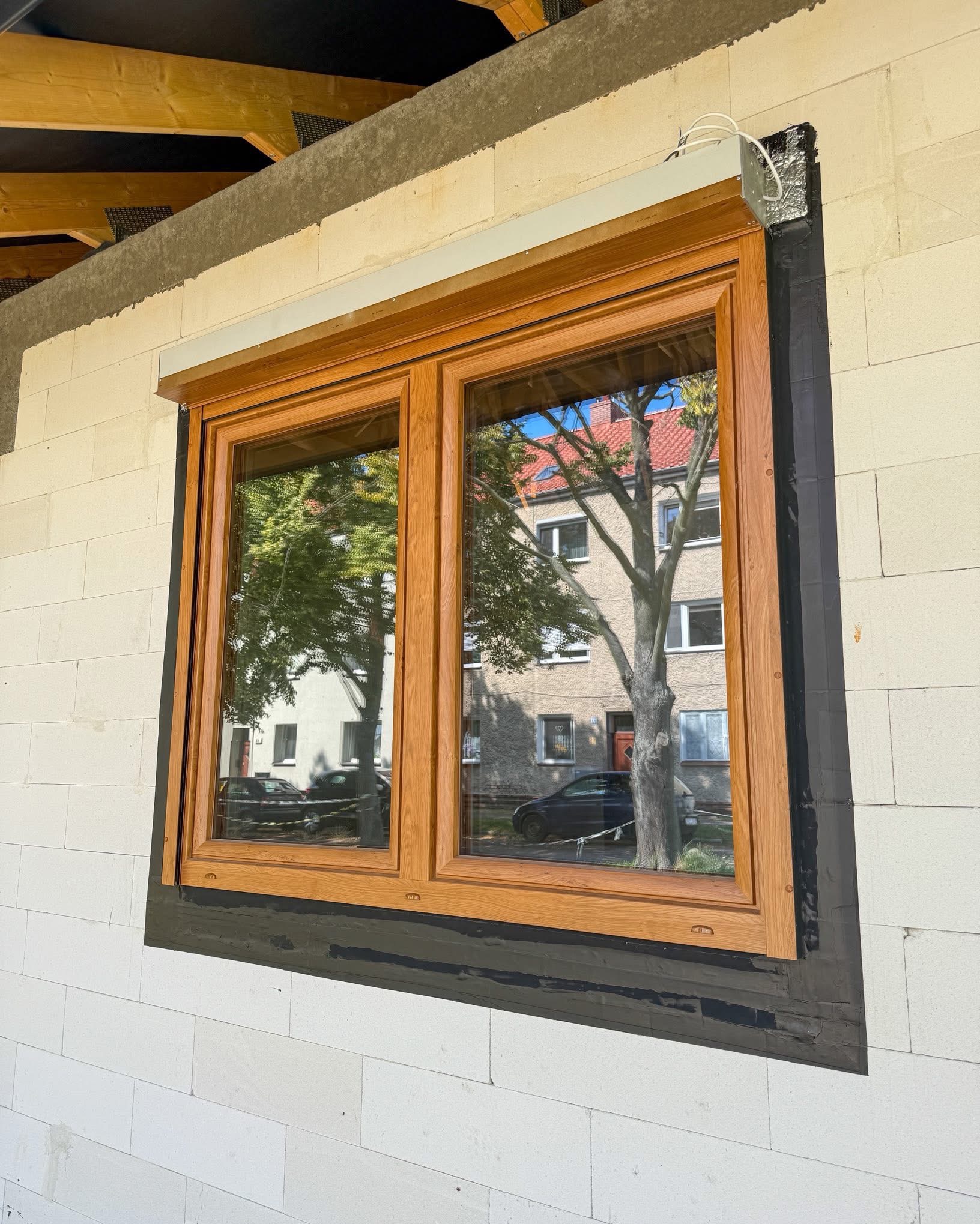 Drewniane okno z roletą zewnętrzną w trakcie montażu w ścianie z betonu komórkowego. Widoczne uszczelnienie wokół ramy okiennej.