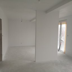 Vladyslav Zabrodin - Białe, świeżo pomalowane wnętrze z widocznym wałkiem malarskim przy oknie. Surowy beton na podłodze, przygotowane do dalszych prac wykończeniowych.