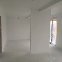 Białe, świeżo pomalowane wnętrze z widocznym wałkiem malarskim przy oknie. Surowy beton na podłodze, przygotowane do dalszych prac wykończeniowych.