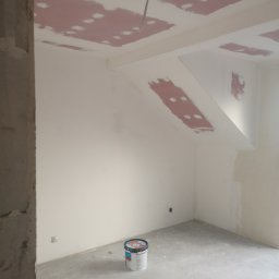 Vladyslav Zabrodin - Wnętrze w trakcie prac wykończeniowych: ściany i sufit po szpachlowaniu, widoczne łączenia płyt gipsowych, na podłodze stoi wiadro z farbą. Surowy stan.