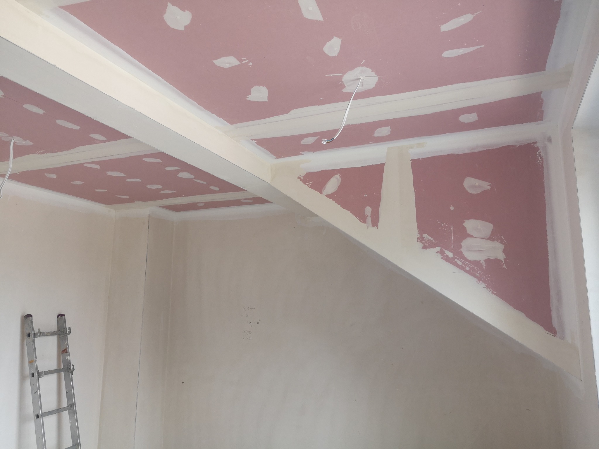 Skośny sufit z płyt karton-gips, częściowo wyszpachlowany, z widocznymi łączeniami i przewodami. W rogu drabina malarska. Ściany przygotowane do malowania.