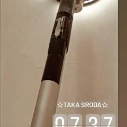 Mateusz 2TUR - Szlifierka do gładzi marki Festool w trakcie pracy na jasnej ścianie. Widoczny pył i ślady szlifowania. Ujęcie z dołu, narzędzie skierowane ku górze.