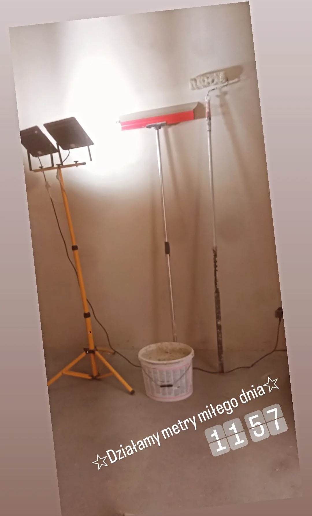 Stanowisko pracy: lampa na statywie, wiadro z zaprawą, szpachla i wałek malarski oparte o ścianę. Przygotowanie do prac wykończeniowych.