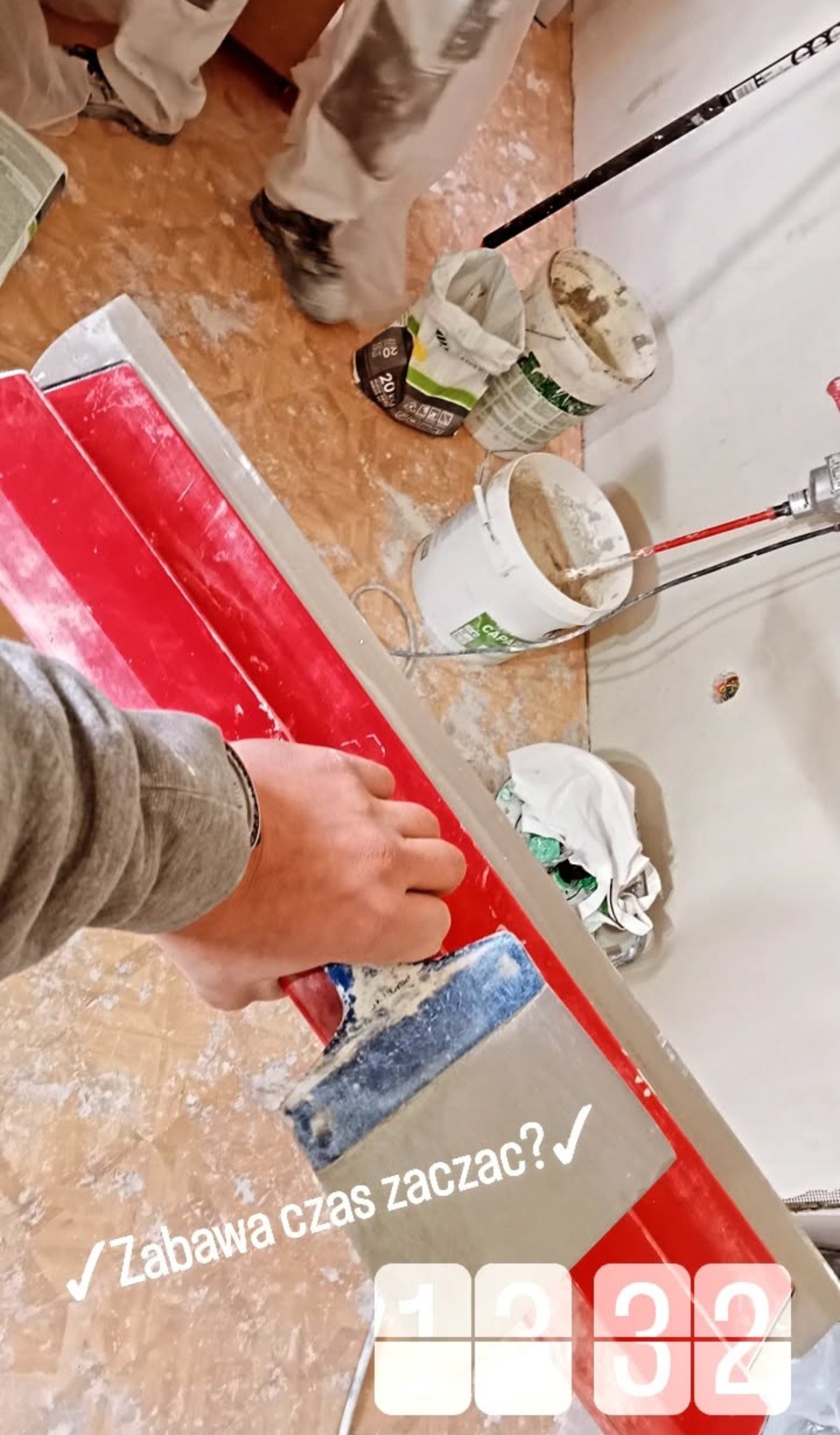 Praca z pacą na ścianie, widoczne wiaderka z masą i narzędzia. Przygotowania do nakładania gładzi. Podłoga zabezpieczona przed zabrudzeniem. Ujęcie z góry.