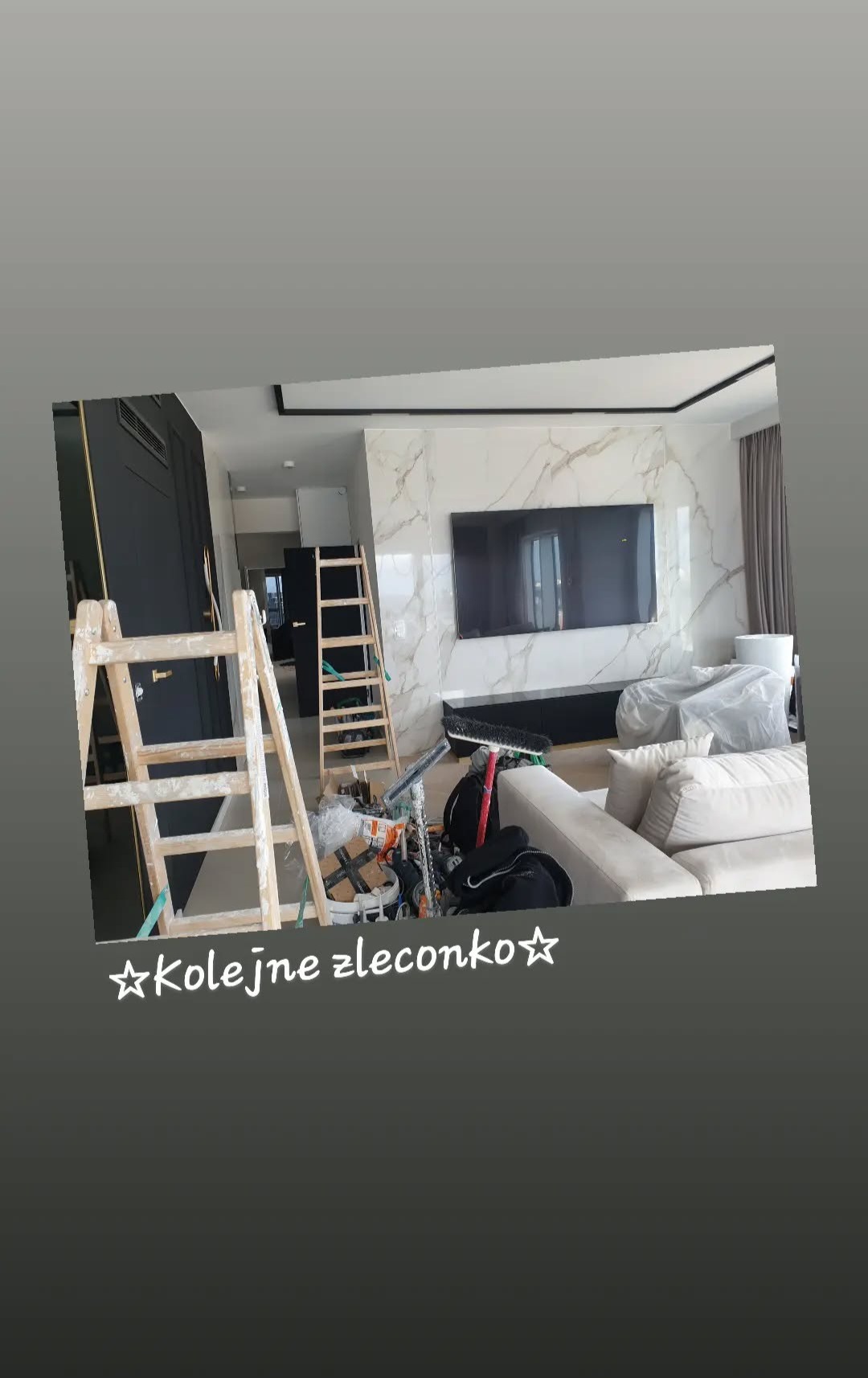 Salon w trakcie prac wykończeniowych: drabiny malarskie, zabezpieczony mebel, ściana z marmurowym wzorem i telewizor. Widok na otwarte przejście do dalszej części mieszkania.
