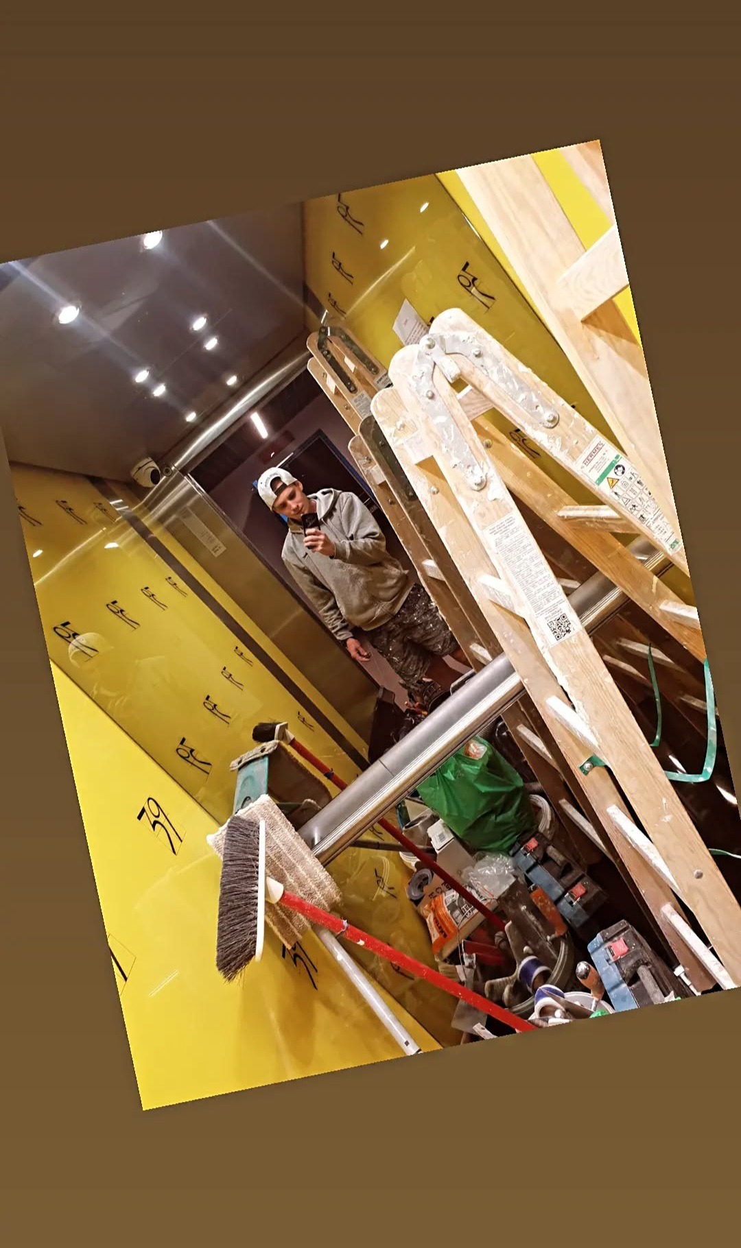 Pracownik robi zdjęcie telefonem w trakcie prac wykończeniowych. Widoczna drabina, narzędzia i zabezpieczona folią ściana w kolorze żółtym.