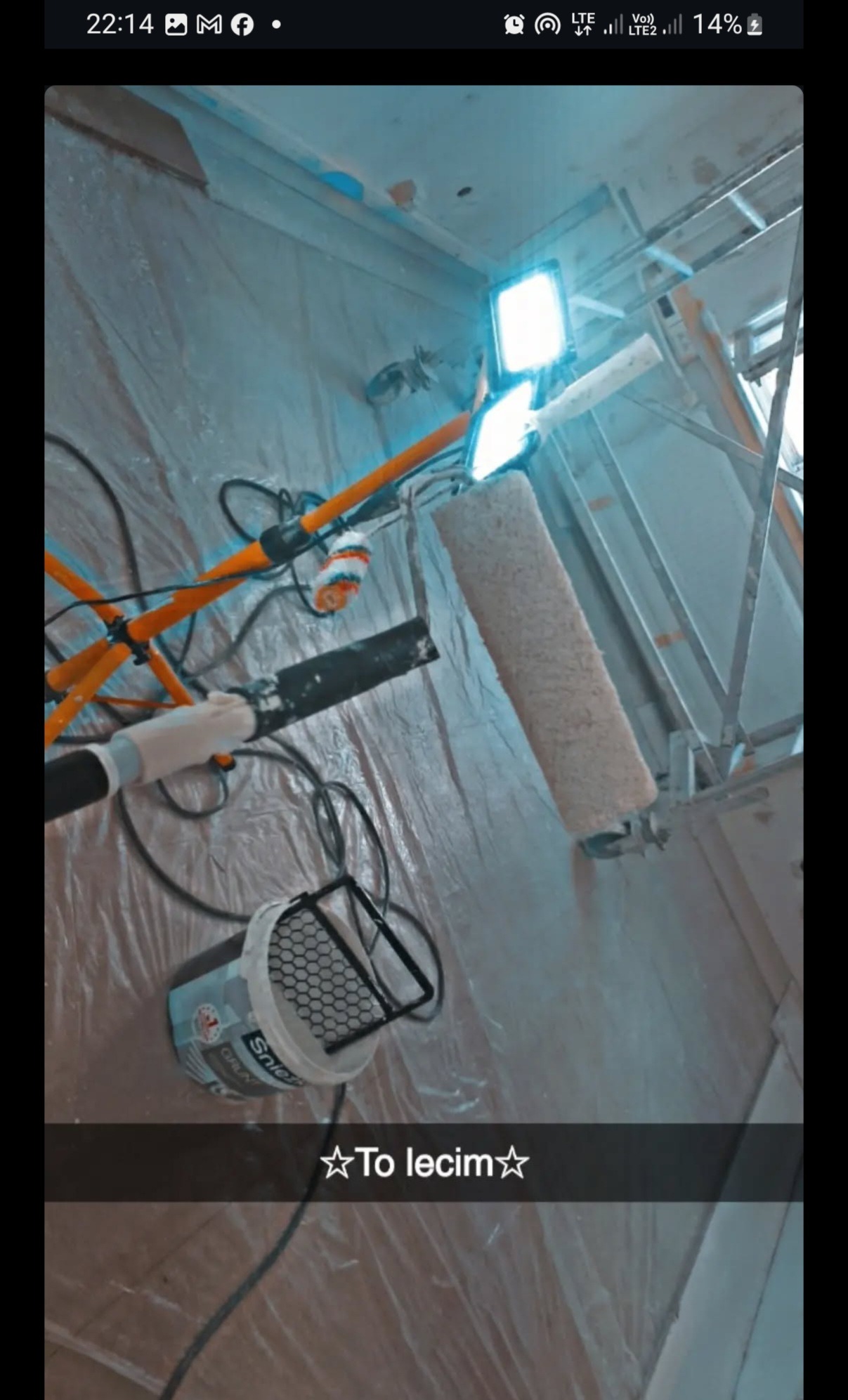 Przygotowanie do malowania ścian: wałek, farba, oświetlenie na statywie i folia ochronna. Widok z dołu, podkreślający profesjonalne wyposażenie.