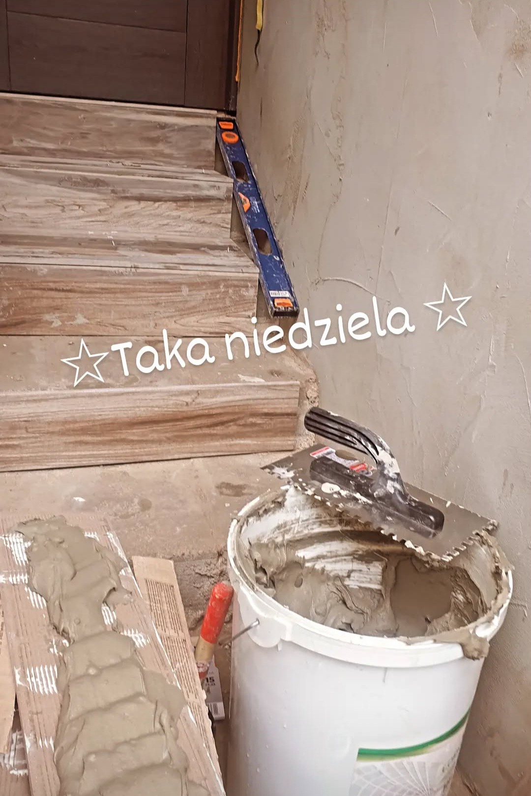 Wykończone płytkami schody z poziomicą. Obok wiadro z zaprawą i kielnia. Prace wykończeniowe w trakcie realizacji. Widoczna surowa ściana.