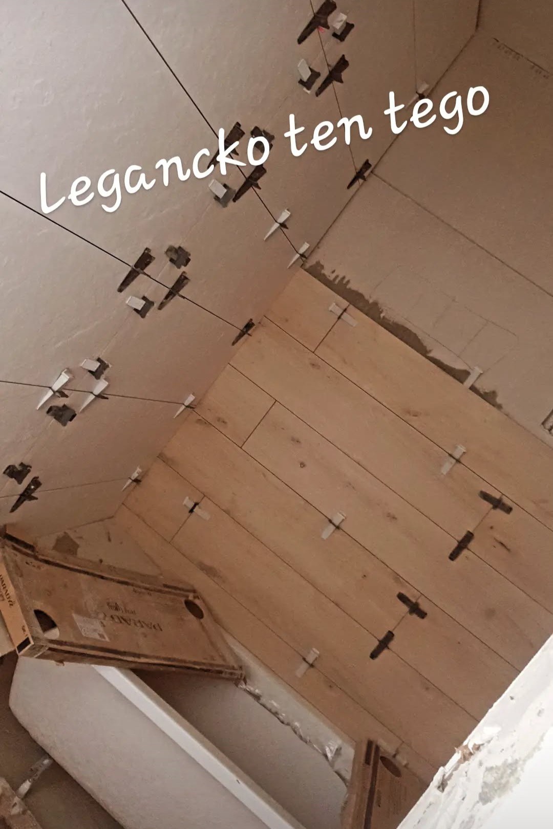 Układanie drewnopodobnych paneli na ścianie z użyciem krzyżyków dystansowych i sznurków poziomujących. Widoczna kartonowa paczka paneli.