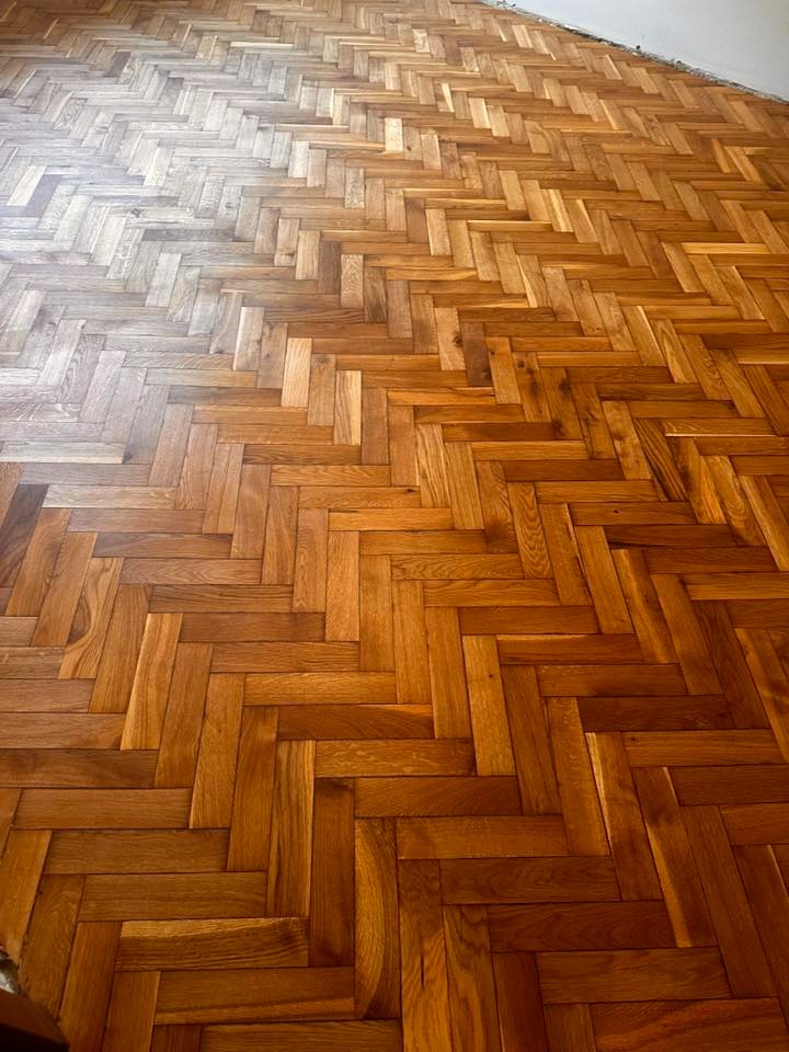 Parkiet ułożony w jodełkę po cyklinowaniu w Łodzi. Widoczna różnica w kolorze drewna przed i po renowacji, ukazująca efekt odświeżenia i przywrócenia blasku podłodze.